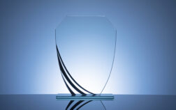 Elegant blank glass shield trophy on dark blue background ready to be engraved for the winner of a competition or race